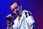 Freddie Mercury impersonator performing live in a white jacket with microphone.