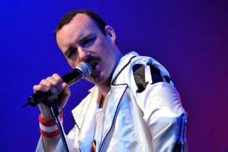 Freddie Mercury impersonator performing live in a white jacket with microphone.