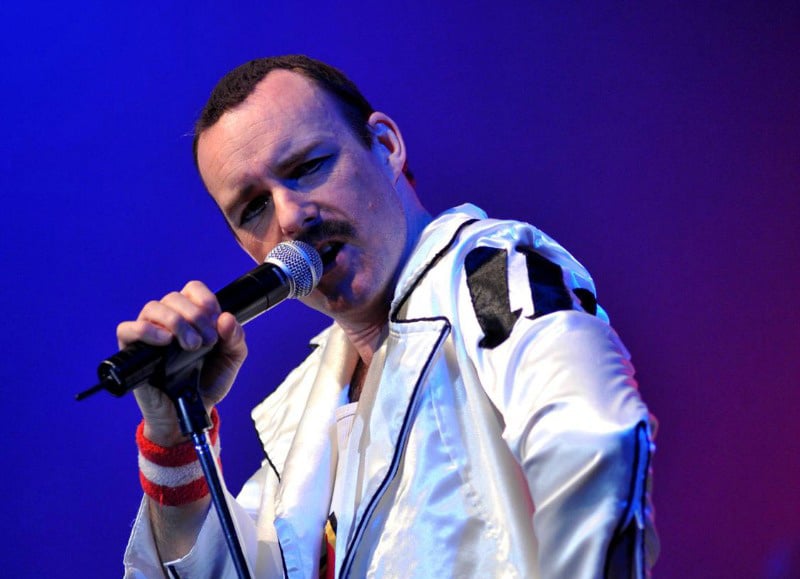 Freddie Mercury impersonator performing live in a white jacket with microphone.