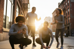Group of friends getting ready for a morning run, checking phones and tying shoes as part of the 'Check your pals then run ritual' wellness trend