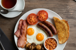 A plated Full English breakfast with eggs, bacon, sausages, tomatoes, mushrooms, beans, and fried bread.