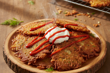 Crispy homemade potato latkes with sour cream and Franks RedHot on a plate.